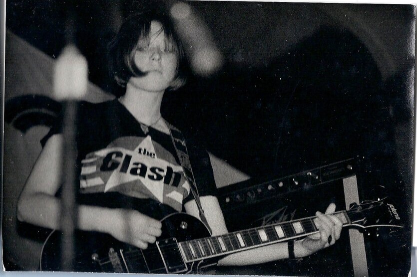 Eine junge Frau mit Gitarre und T-Shirt der Punkband "The Clash"