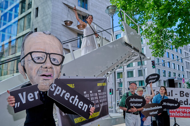 Protest vor dem Aussenministerium in Berlin, eine Merz-Puppe bricht ein Schild auf dem "Versprechen" steht, andere tragen kleinere Schilder ""Aufnahmen fortsetzen"