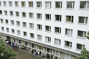 Menschen in der Warteschlange vor dem Bürgeramt Neukölln, Donaustrasse 29, ein weißer Neubaublock