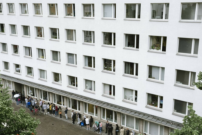 Menschen in der Warteschlange vor dem Bürgeramt Neukölln, Donaustrasse 29, ein weißer Neubaublock