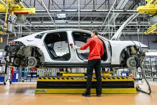 Ein Mitarbeiter montiert einen Porsche Panamera im Werk Leipzig, der Porsche steht noch ohne Reifen, Türen und Fenster auf einer Hebebühne vor der ein ARbeiter steht