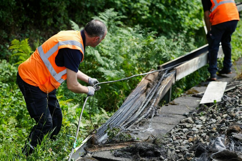 Zwei Männer in Warnwesten stehen an einem Schacht, in dem verbrannte oder angebrannte Kabel liegen
