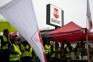 Mitarbeiter*innen demonstrieren in Warnwesten vor ihrem Betrieb