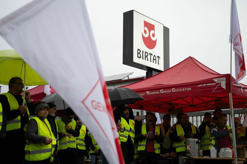 Mitarbeiter*innen demonstrieren in Warnwesten vor ihrem Betrieb