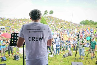 Michael Ballweg hält eine Rede, Rückenansicht, er spricht zum Publikum - auf seinem T-Shirt s teht: www.querdenken-711.de und das Wort CREW