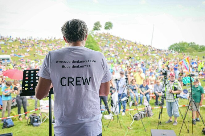 Michael Ballweg hält eine Rede, Rückenansicht, er spricht zum Publikum - auf seinem T-Shirt s teht: www.querdenken-711.de und das Wort CREW