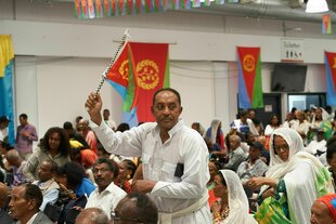 Besucher des Eritrea-Festivals sitzen in der Gießener Messehalle. Ein Mann steht und schwenkt eine eritreische Flagge
