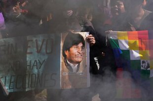 Dichter Rauch umhüllt Demonstrierende, die Transparente und Fahnen hochhalten – darunter ein Porträt von Evo Morales und ein Schild mit der Aufschrift: „Sin Evo no hay elecciones“.