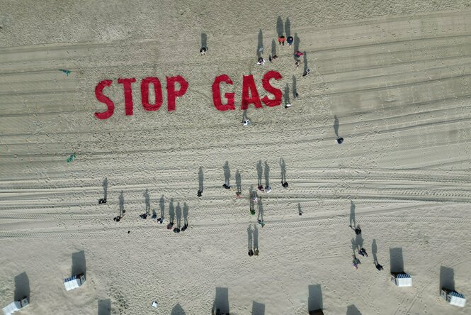 Roter Schriftzug "Stop Gas" auf weißem Sand, dazu Schatten von Menschen und Strandkörben
