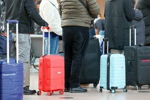 menschen mit kleinen Rollkoffern in der Schlange