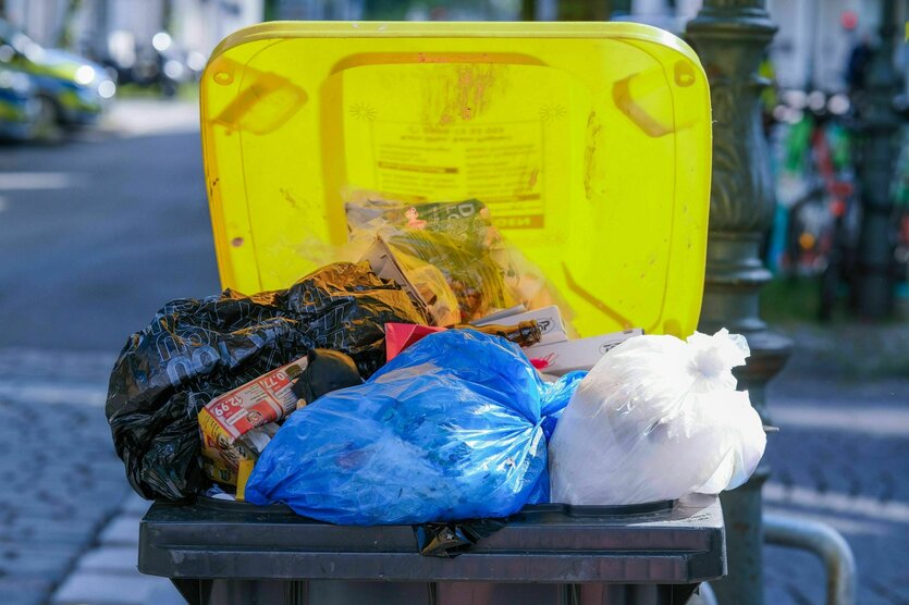 Überquellende, gelbe Plastikmülltonne mit mehreren Müllsäcken