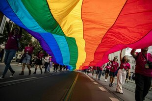 Menschen beim Berliner CSD tragen eine überdimensionierte Regenbogenfahne auf der Straße