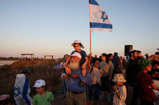 Mann trägt Kind auf den Schultern, im Hintergrund eine Israel-Flagge
