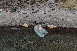 Ein plattes Schlauchboot und Rettungsreifen liegen zwischen Müll am Strand
