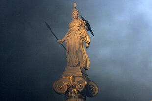 Statue der griechischen Göttin Athene mit Speer, Schild und Helm, auf einer Säule stehend und von dunklen Wolken umgeben.