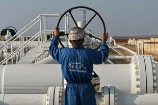 Ein Mann mit Schutzhelm und blauem Arbeiteranzug steht an einer Gaspipeline und dreht an einem großen Rad