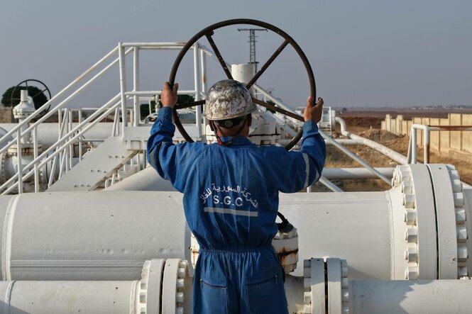 Ein Mann mit Schutzhelm und blauem Arbeiteranzug steht an einer Gaspipeline und dreht an einem großen Rad
