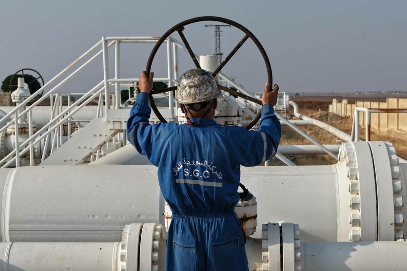 Ein Mann mit Schutzhelm und blauem Arbeiteranzug steht an einer Gaspipeline und dreht an einem großen Rad