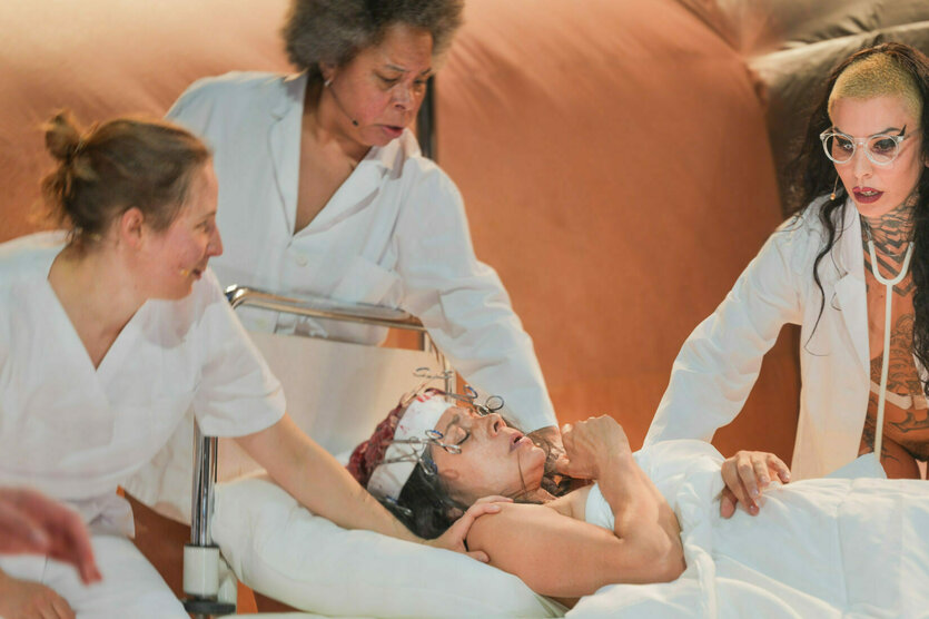 Eine Bühnenszene des aktuellen Theaterstücks von Florentina Holzinger zeigt vier Performerinnen, die um ein Krankehausbett stehen