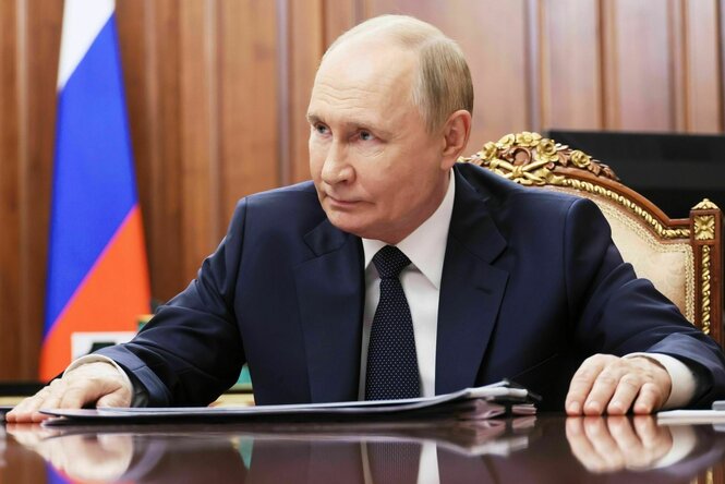 Ein Mann (Wladimir Putin) sitzt an einem Schreibtisch und schaut ernst