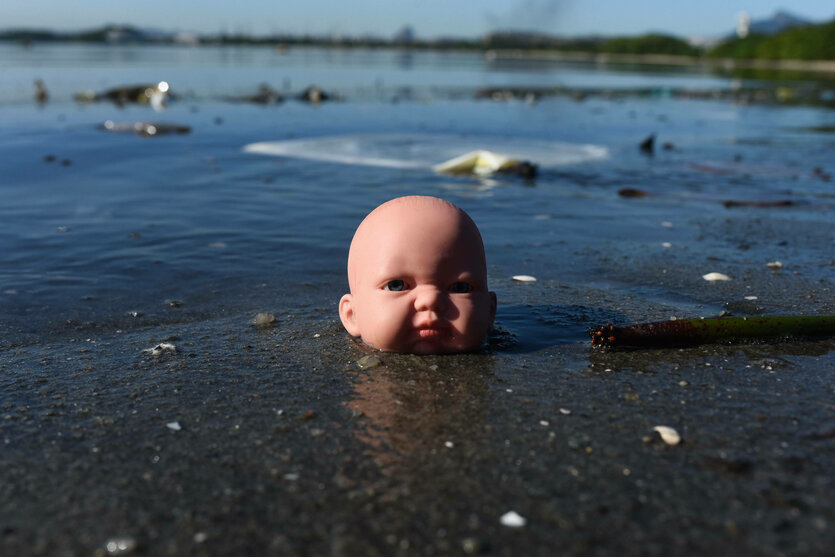 Ein alter puppenkopf aus Plastik liegt im seichten Wasser