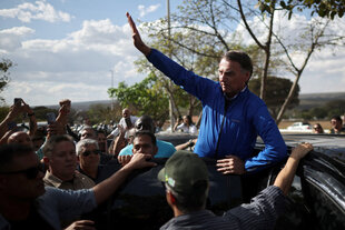 Bolsonaro steigt aus einem Auto, er hat eine Hand zum Gruß erhoben, um ihn herum eine Menschenmenge