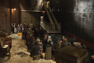 Menschen-Puppen in historischen Kleidern stehen in einer Schlange vor einem Schiff.