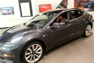 Ein Tesla in einem Autoschauhaus, in dem Peter Unfried sitzt, seine Hand vor dem Gesicht.