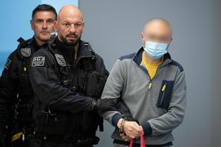 Ein Mann wird von Sicherheitsbeamten in einen Gerichtssaal begleitet