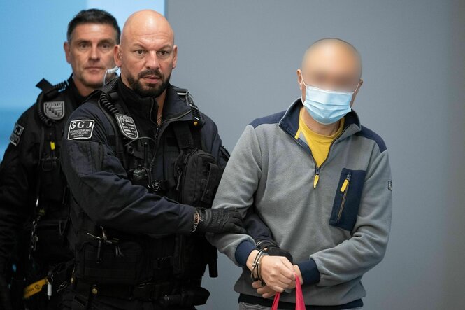 Ein Mann wird von Sicherheitsbeamten in einen Gerichtssaal begleitet