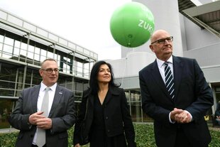 Sommertour im Mantel. Katherina Reiche steht zwischen zwei Anzugträgern, einem großen Mann und einem eher kleinen Mann. Hinter ihnen fliegt ein Luftballon mit der aufschrift: Gas für unsere Zukunft