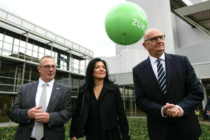 Sommertour im Mantel. Katherina Reiche steht zwischen zwei Anzugträgern, einem großen Mann und einem eher kleinen Mann. Hinter ihnen fliegt ein Luftballon mit der aufschrift: Gas für unsere Zukunft