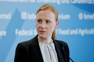 Eine Frau mit weißer Bluse und schwarzem Jacket schaut ernst