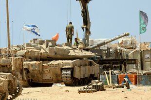 Zwei israelische Soldaten stehen auf Panzern, die auf staubigem Boden stehen, eine Israelflagge weht im Wind