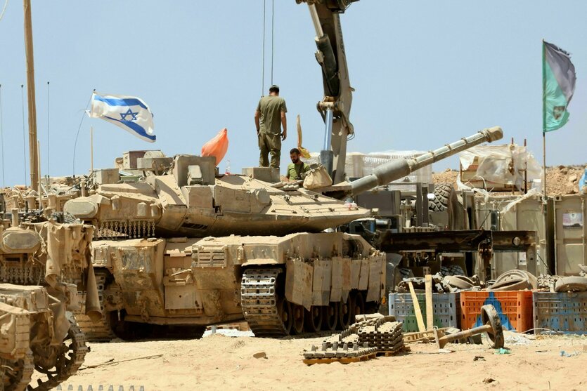 Zwei israelische Soldaten stehen auf Panzern, die auf staubigem Boden stehen, eine Israelflagge weht im Wind