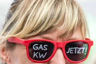 Eine Frau trägt eine rote Brille auf der mit weißer Schrift steht: GAS KW JETZT!