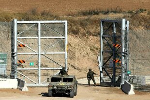 Grenze zu Gaza: zwei israelische Soldaten fahren mit ihrem Jeep über die Grenze, die von einem hohen Metallzaun gesichert wird, einer der Soldaten schließt die Tür des Zauns