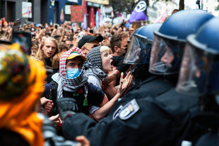 Behelmte Polizisten drängen Menschen mit Kufija auf einer Demonstration zurück