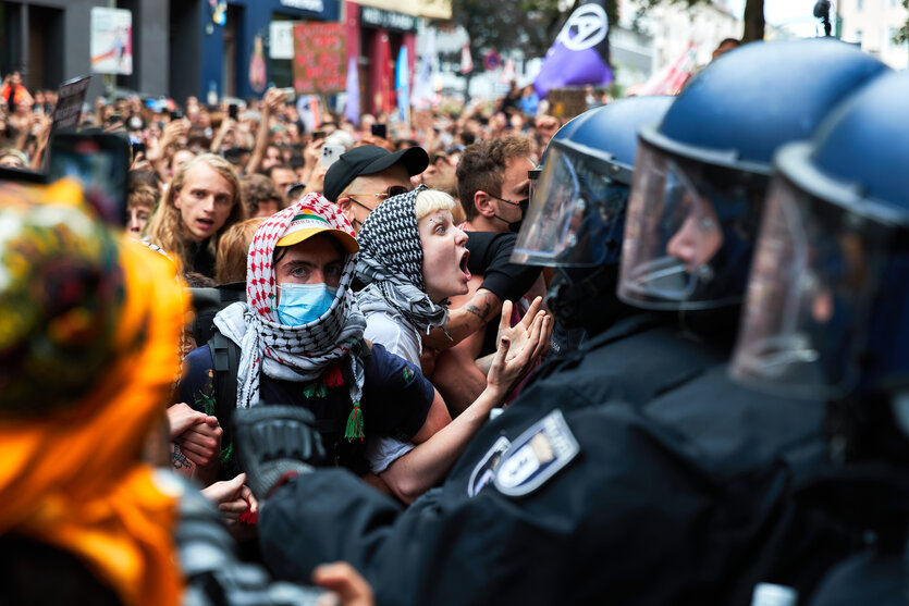 Behelmte Polizisten drängen Menschen mit Kufija auf einer Demonstration zurück