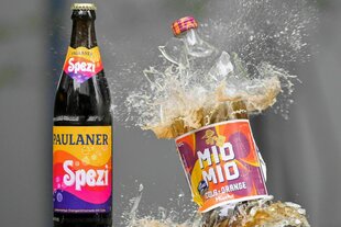 Eine Spezi-Flasche des Herstellers Paulaner (l) steht neben einer zerberstenden Flasche Mio-Mio-Cola-Orange-Mische des Herstellers Berentzen (r)