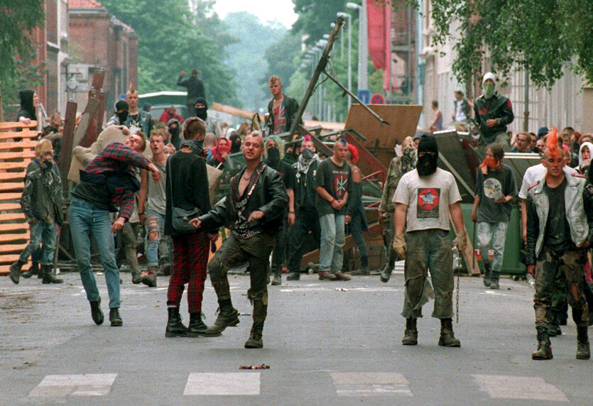 Eine Straßenszene während der Chaostage 1995 in Hannover: Punks, viele von ihnen mit Springerstiefeln und Irokesen, vor und hinter einer Straßenbarrikade aus Müllcontainern, Masten und Brettern