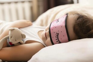 Ein Mädchen schläft mit einem Kuscheltier in einem Bett