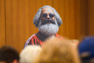 Ein Darsteller mit Karl-Marx-Maske und Sonnenbrille auf einer Bühne