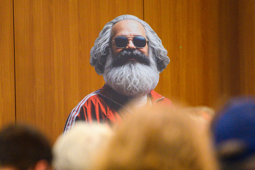 Ein Darsteller mit Karl-Marx-Maske und Sonnenbrille auf einer Bühne