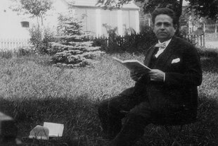 Kurt Tucholsky sitzt in einem Garten und hält ein Buch in der Hand