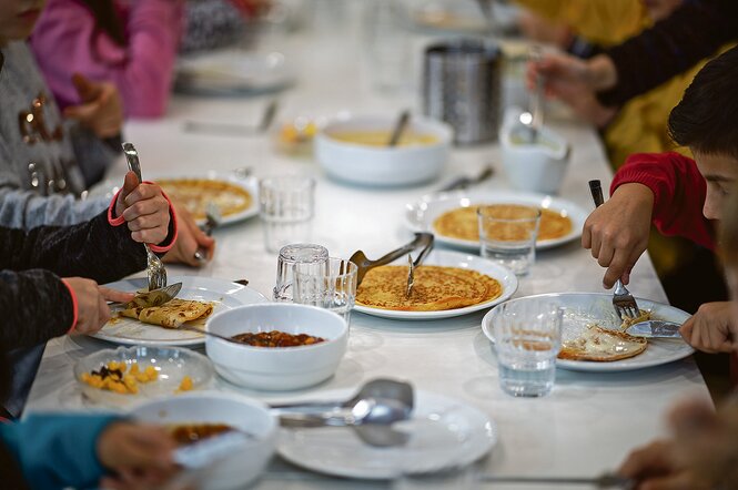 Kinder sitzen an einem Tisch und essen Pfannkuchen.