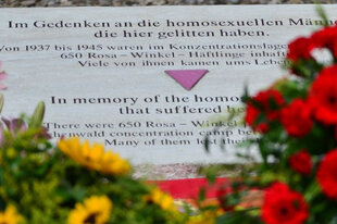 Eine Aufnahme des Gedenksteins für homosexuelle Opfer der Nazis beim ehemaligen KZ Buchenwald, der Gedenkstein ist von Blumenbouquets umgeben.
