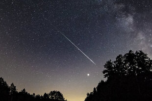 Der Sternenhimmel in Langzeitbelichtung, eine Sternschnuppe fliegt übers Firmament.