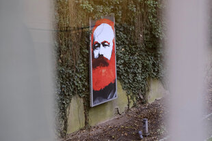 Das colorierte Porträt eines Mannes lehnt an einer Wand, die mit Efeu bewachsen ist