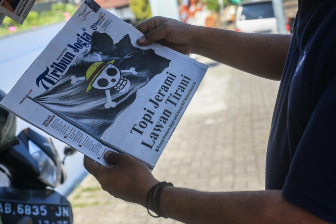 Eine Person zeigt eine Tageszeitung mit One Piece-Illustration